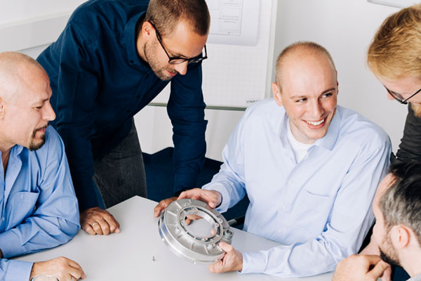 Entwicklung bei GRATZ Ingenieure sitzen am Tisch und reden über produziertes Metallteil