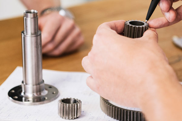 Ferigungsberatung Mehrere gefertigte Metallteile stehen auf einem Tisch und eines davon wird mit der Hand gehalten und näher geprüft.