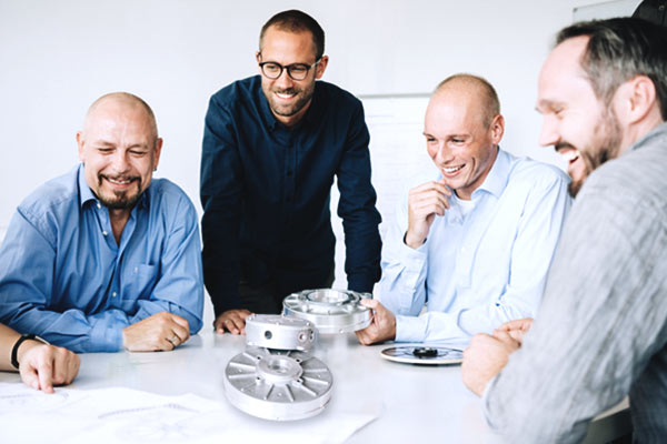 Produktentwicklung Ingenieure sitzen um einen Tisch herum und begutachten selbst entwickelte Metallprodukte