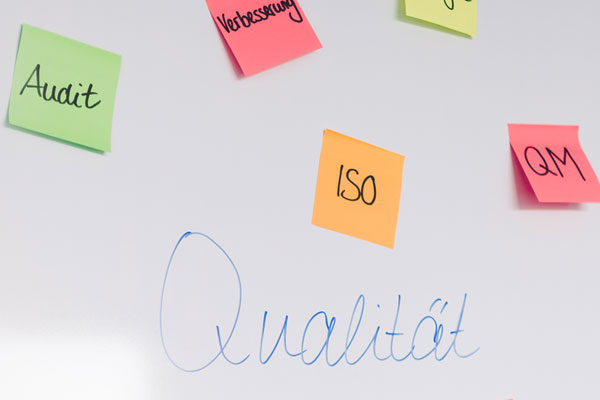 Qualitätsmanagement Whiteboard mit Haftnotizzetteln, auf denen Fachbegriffe zum Thema Qualitätsmanagement stehen.
